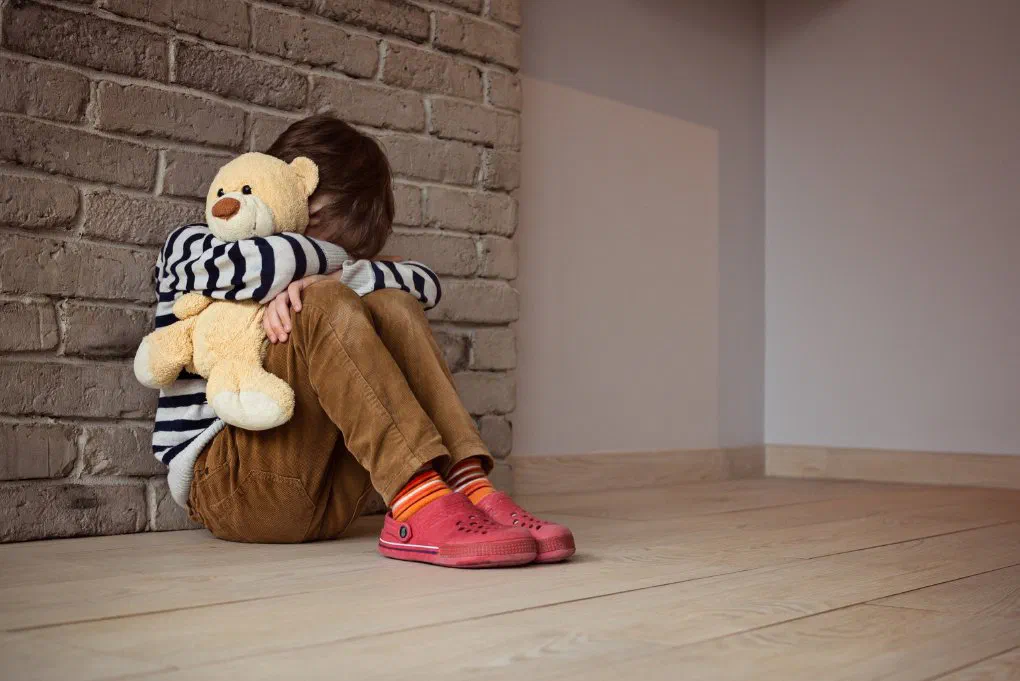 A child holding a teddy bear with head down, illustrating on-site childcare shortfalls